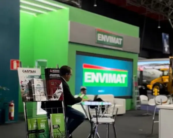 blog estande de feira com painel LED e branding ENVIMAT em estrutura verde, mesa de atendimento em primeiro plano