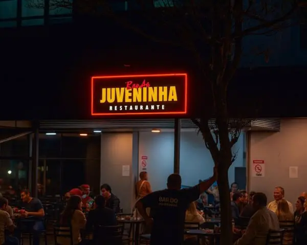 Comunicação visual Fachada noturna com letreiro luminoso vermelho ‘Banda Juveninha Restaurante’ e clientes na área externa